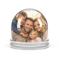 Custom family photo snow globe with a portrait of parents and two children inside, swirling glitter snow in a clear dome