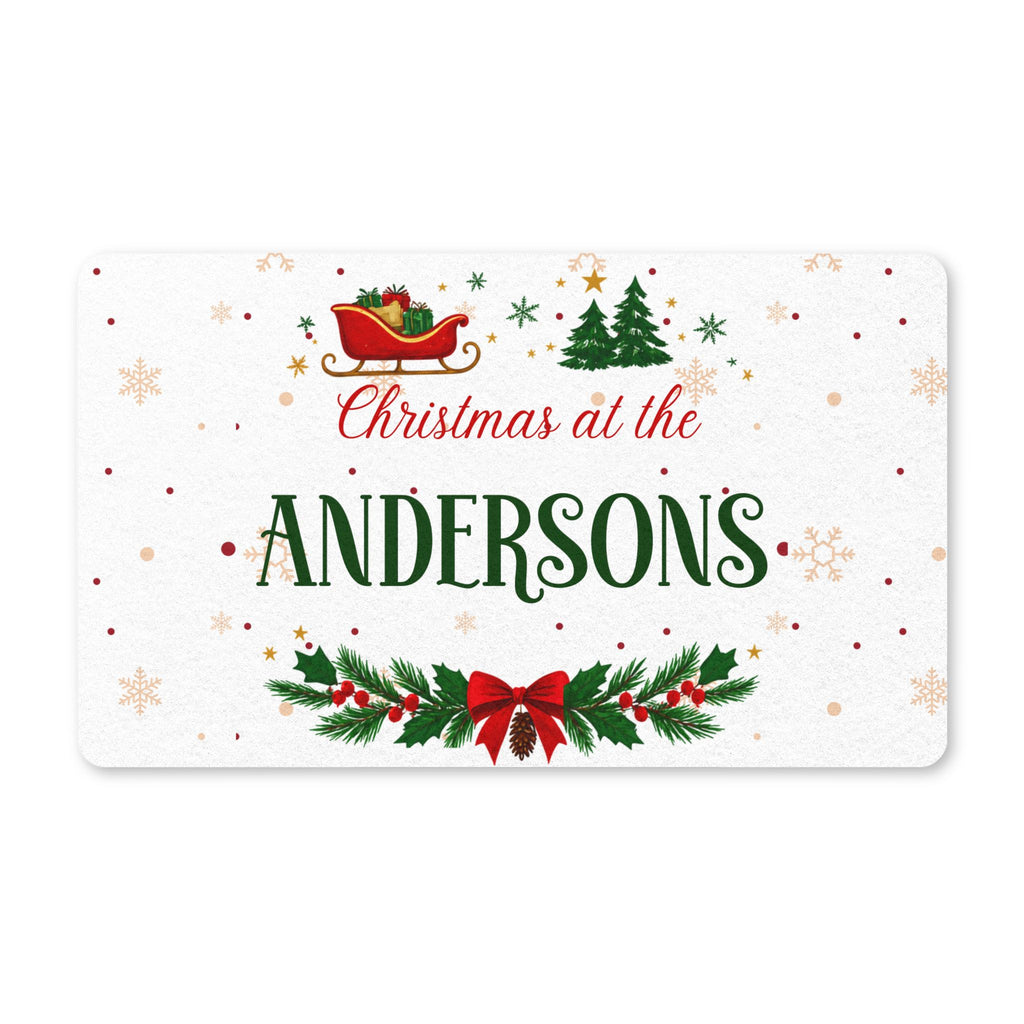 Personalized Christmas doormat with a family name, a red sleigh, evergreen trees and a holly garland on a snowy background